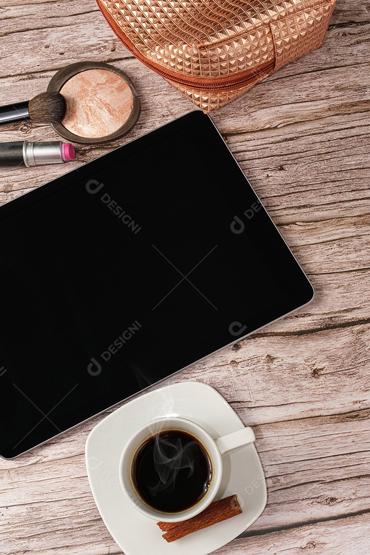 Tablet na mesa cercado por smartphone, batom, pó compacto, xícara de café e maquiagem