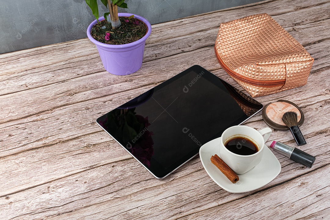 Tablet on table surrounded by smartphone, lipstick, compact powder, coffee cup and makeup