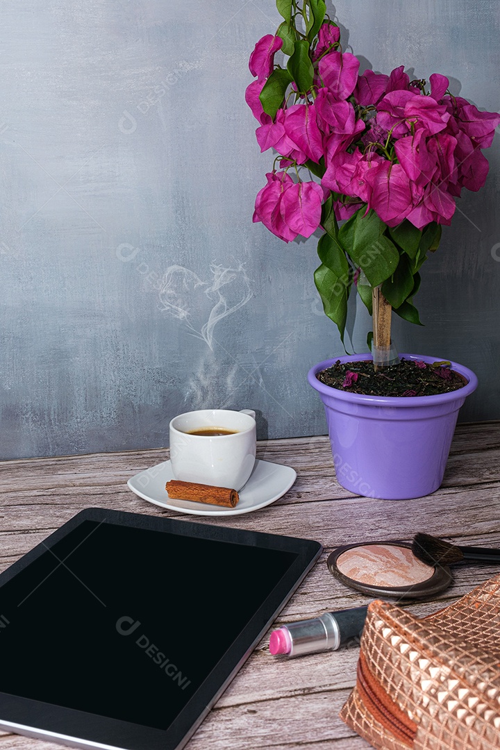 Tablet em cima da mesa cercado por uma xícara de café, batom e foto de maquiagem.