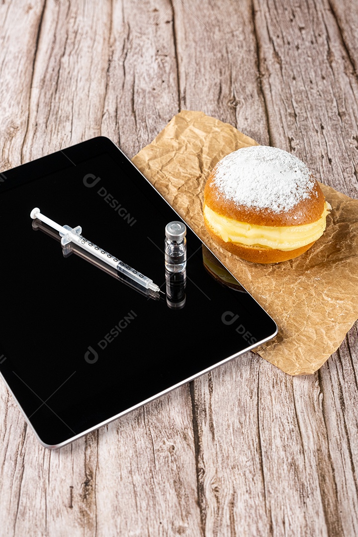 Rosquinhas de creme brasileiras ao lado de uma seringa e ampola com insulina sobre a vista tablet