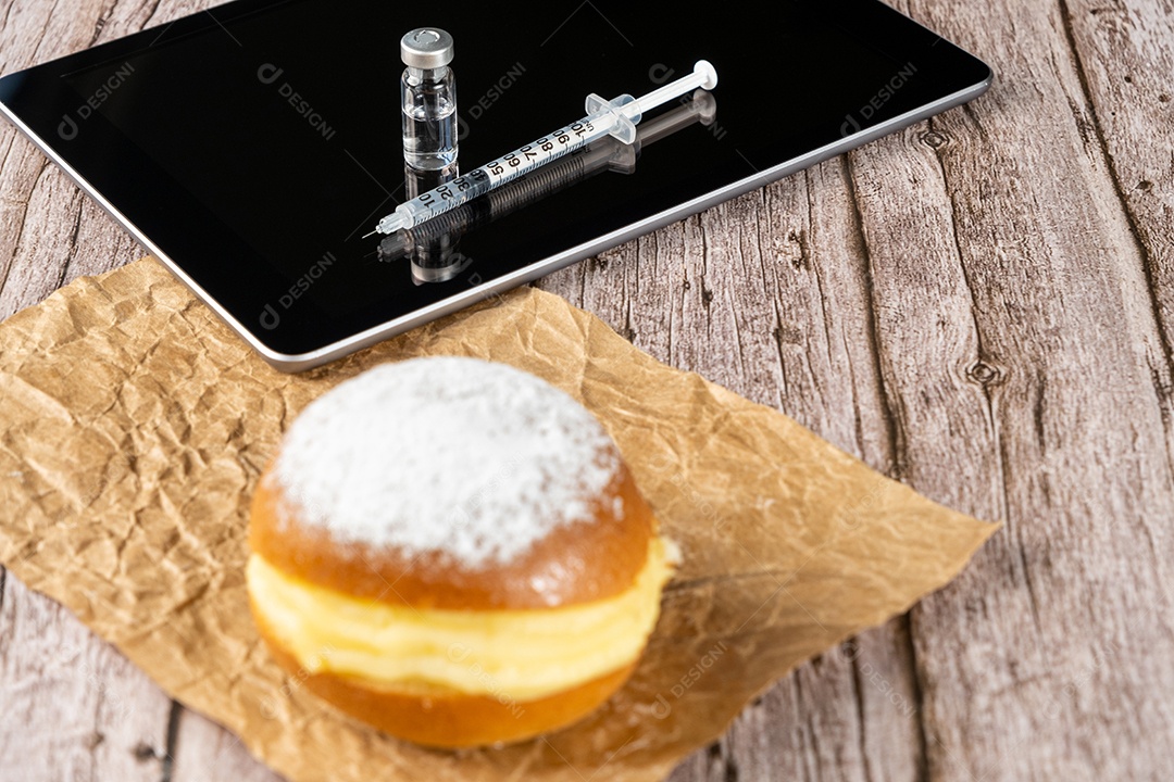 Rosquinhas de creme brasileiras ao lado de uma seringa e ampola com insulina sobre a vista tablet