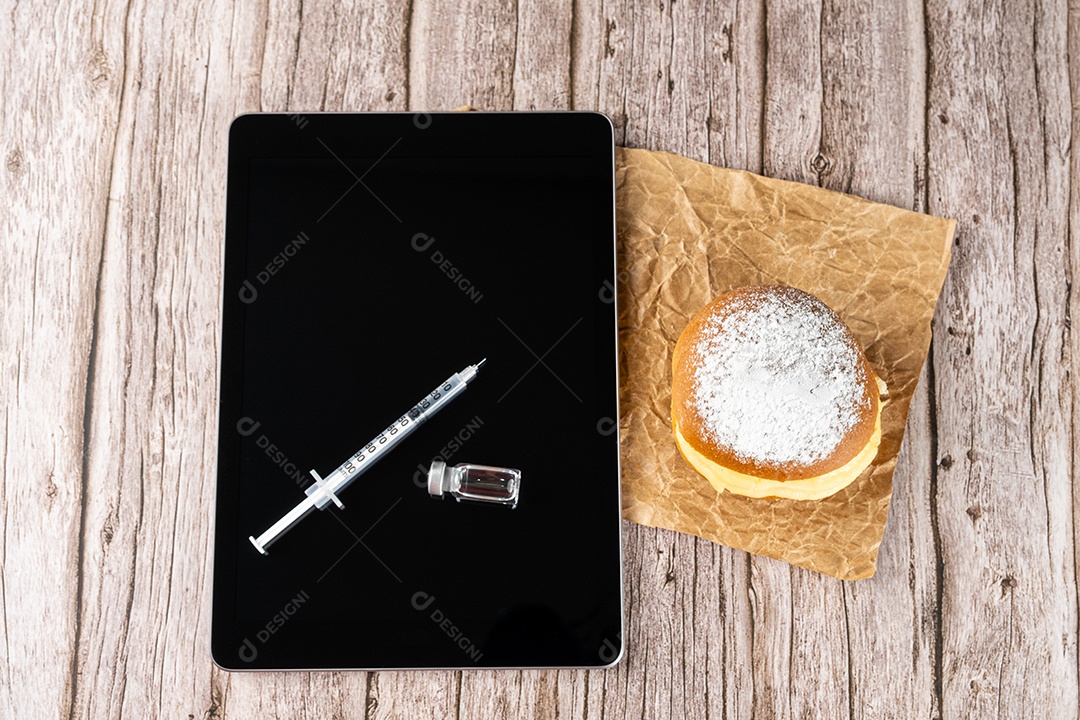 Rosquinhas de creme brasileiras ao lado de uma seringa e ampola com insulina sobre a vista tablet