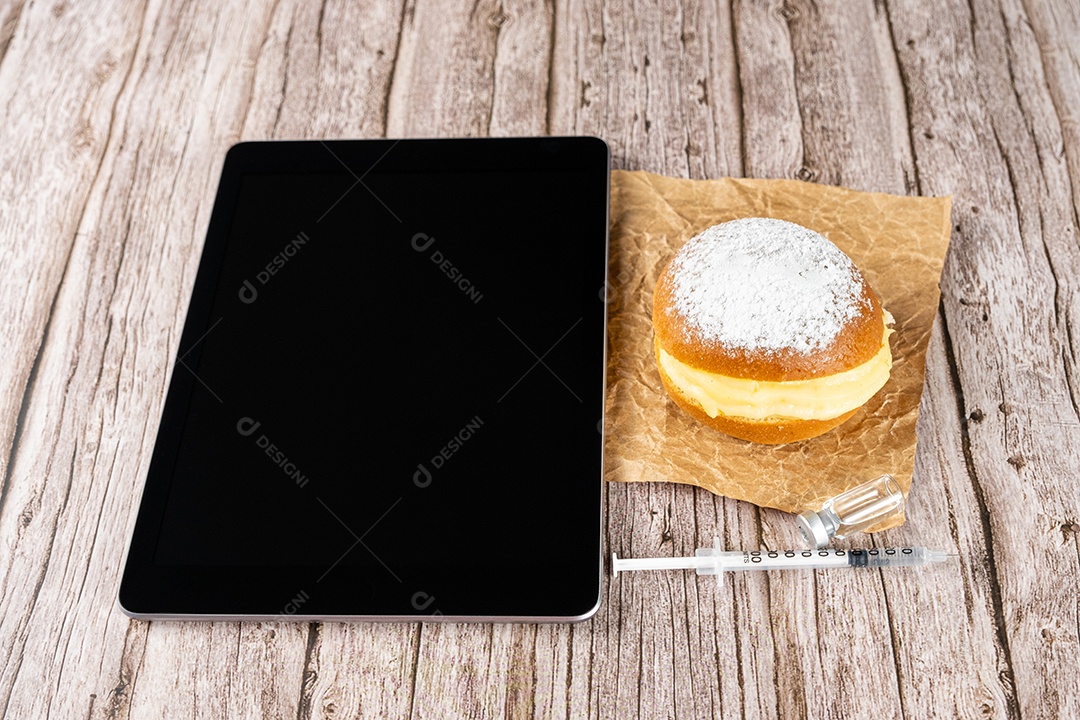 Rosquinhas de creme brasileiras ao lado de uma seringa e ampola com insulina sobre a vista tablet