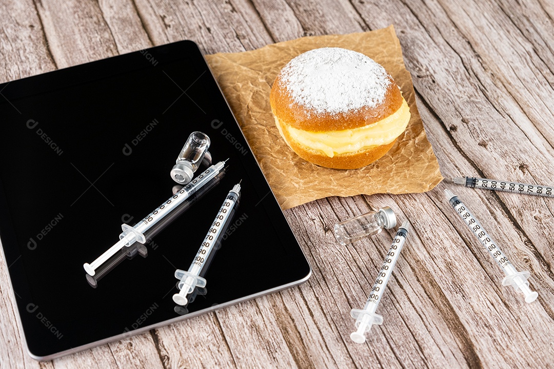 Rosquinhas de creme brasileiras ao lado de uma seringa e ampola com insulina sobre a vista tablet