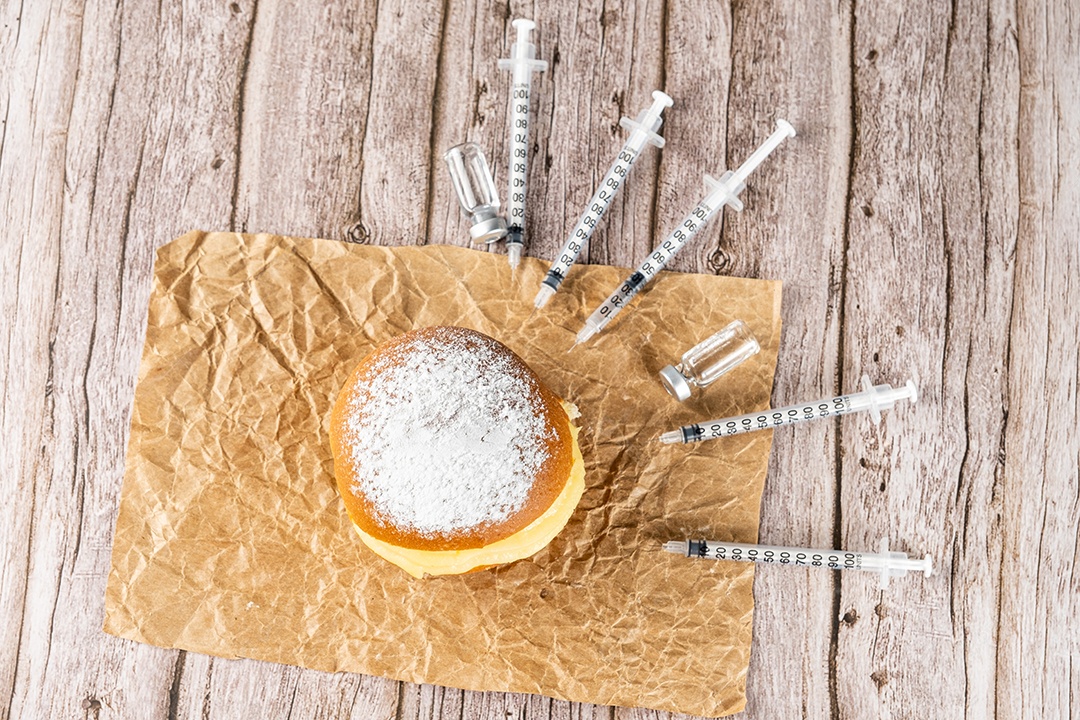 Rosquinhas de creme brasileiras cercadas por várias seringas e ampolas com insulina.