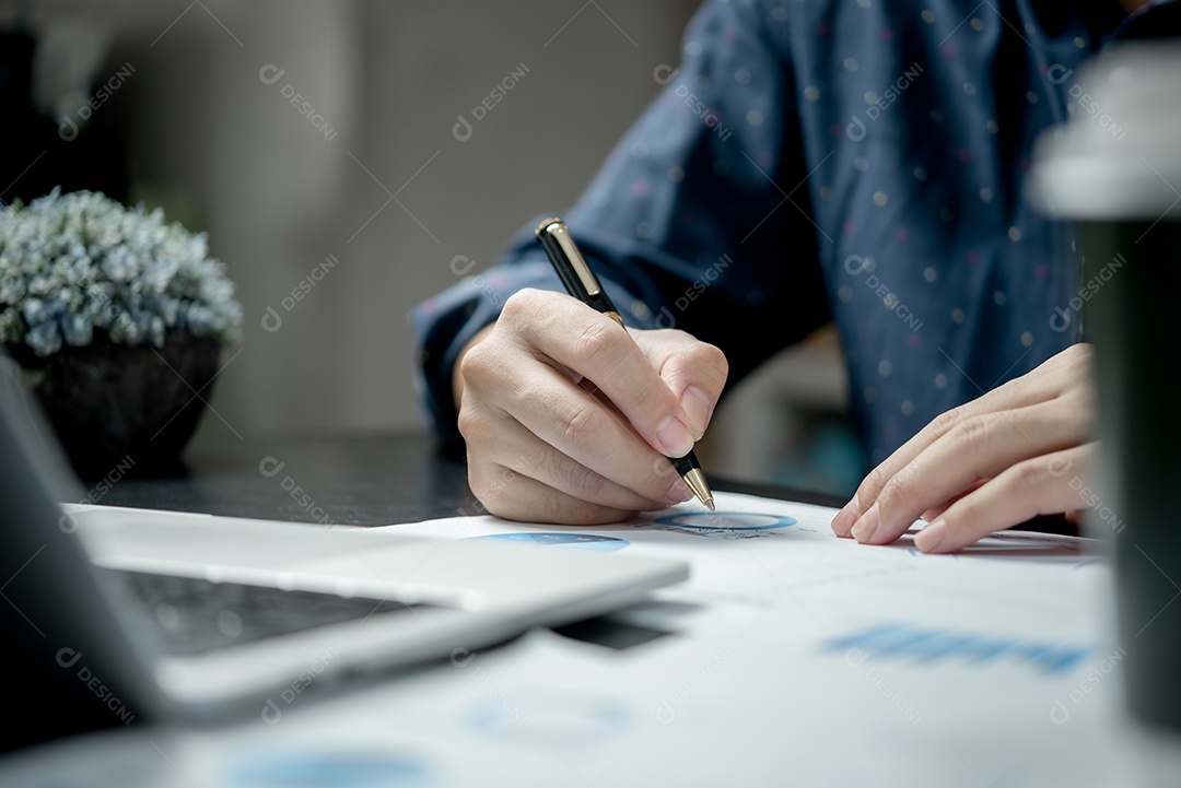 Mãos masculinas com caneta sobre o gráfico do documento e o gráfico na mesa.