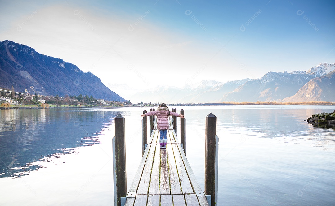 Uma foto de viagem de uma jovem de pé na velha ponte de madeira felizmente no cenário natural do rio no lago próximo à montanha pela manhã.