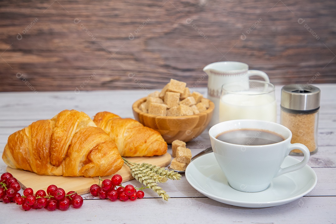 Café da manhã com uma xícara de café preto com pão com croissant e frutas na mesa de madeira.
