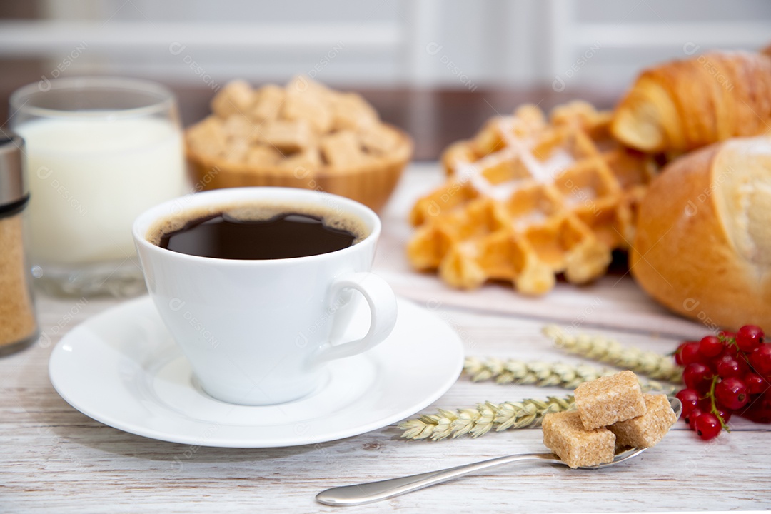 Café da manhã com uma xícara de café preto com pão com croissant e frutas na mesa de madeira.