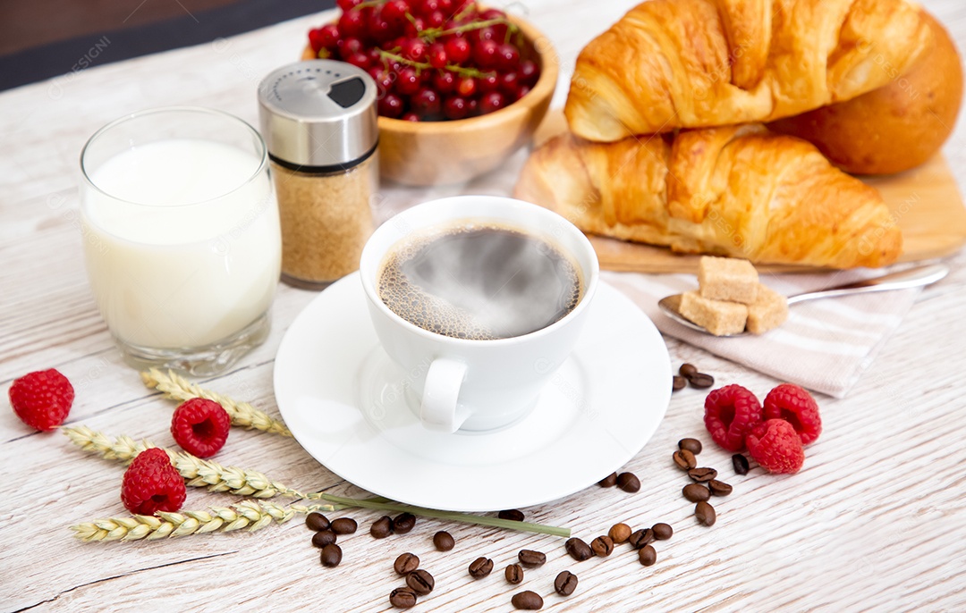 Café da manhã com uma xícara de café preto com pão com croissant e frutas na mesa de madeira.