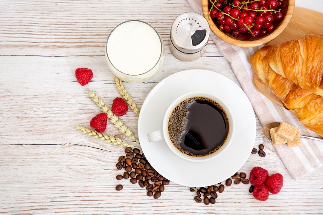 Café da manhã com uma xícara de café preto com pão com croissant e frutas na mesa de madeira.