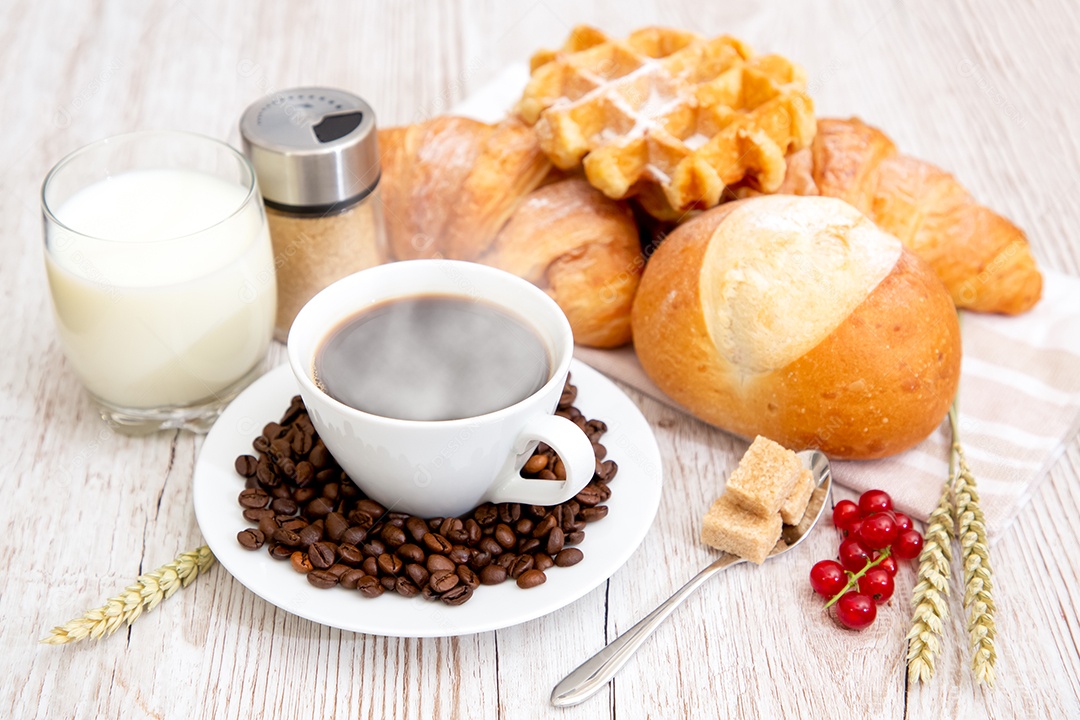 Café da manhã com uma xícara de café preto com pão com croissant e frutas na mesa de madeira.