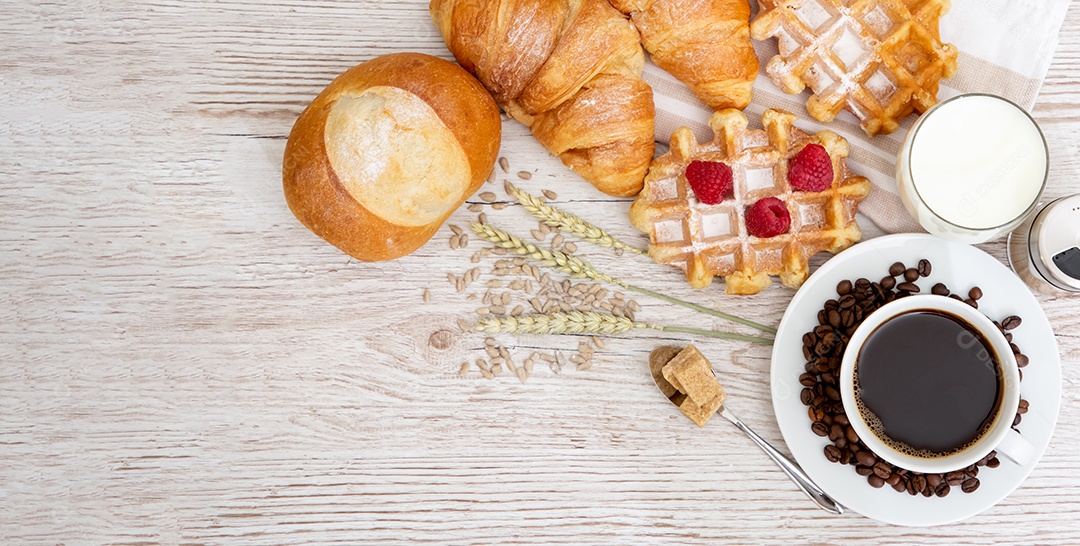 Café da manhã com uma xícara de café preto com pão com croissant e frutas na mesa de madeira.