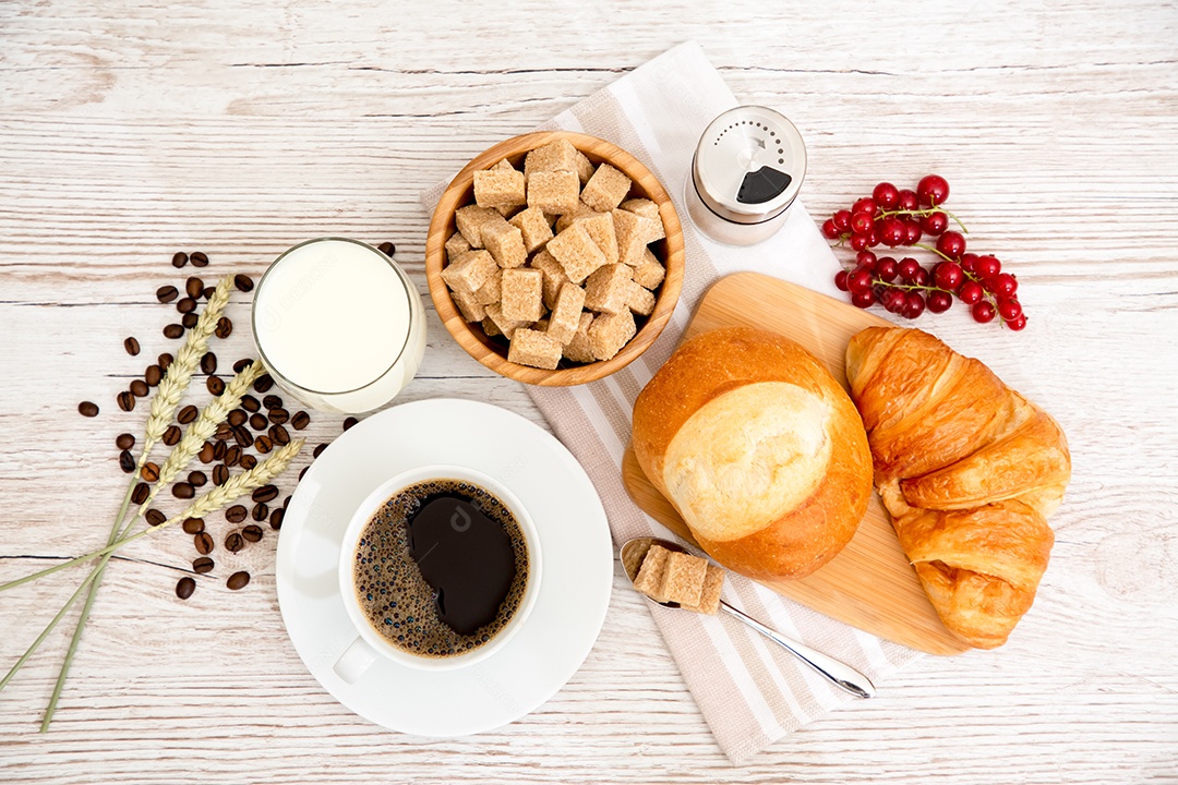 Café da manhã com uma xícara de café preto com pão com croissant e frutas na mesa de madeira.