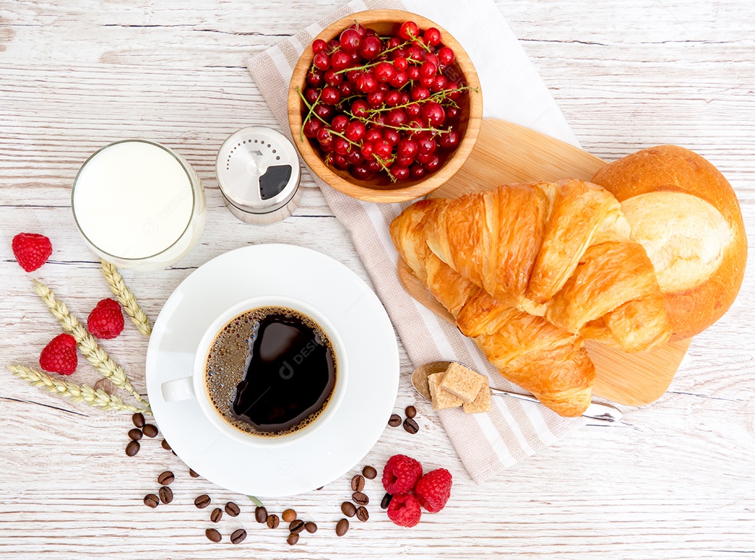 Café da manhã com uma xícara de café preto com pão com croissant e frutas na mesa de madeira.
