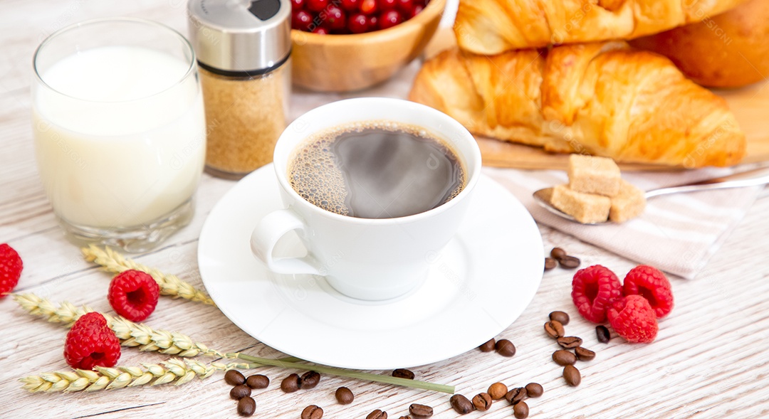 Café da manhã com uma xícara de café preto com pão com croissant e frutas na mesa de madeira.