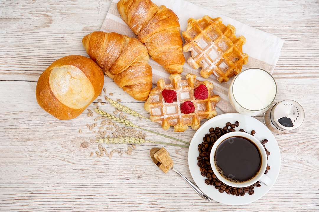 Café da manhã com uma xícara de café preto com pão com croissant e frutas na mesa de madeira.
