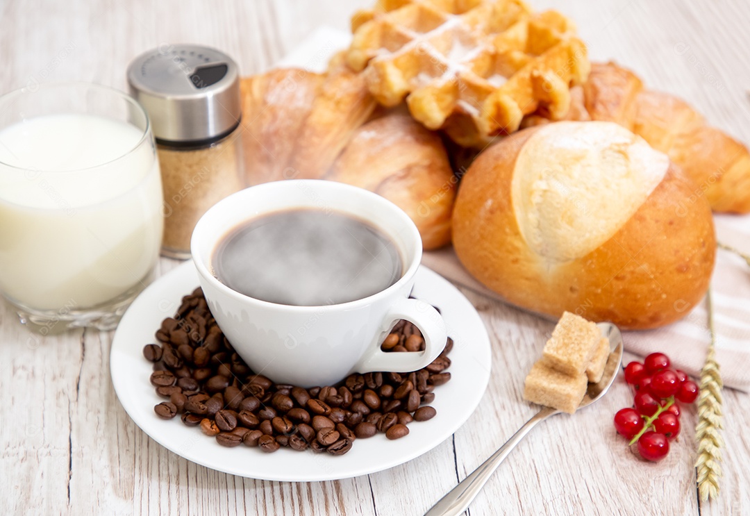 Café da manhã com uma xícara de café preto com pão com croissant e frutas na mesa de madeira.
