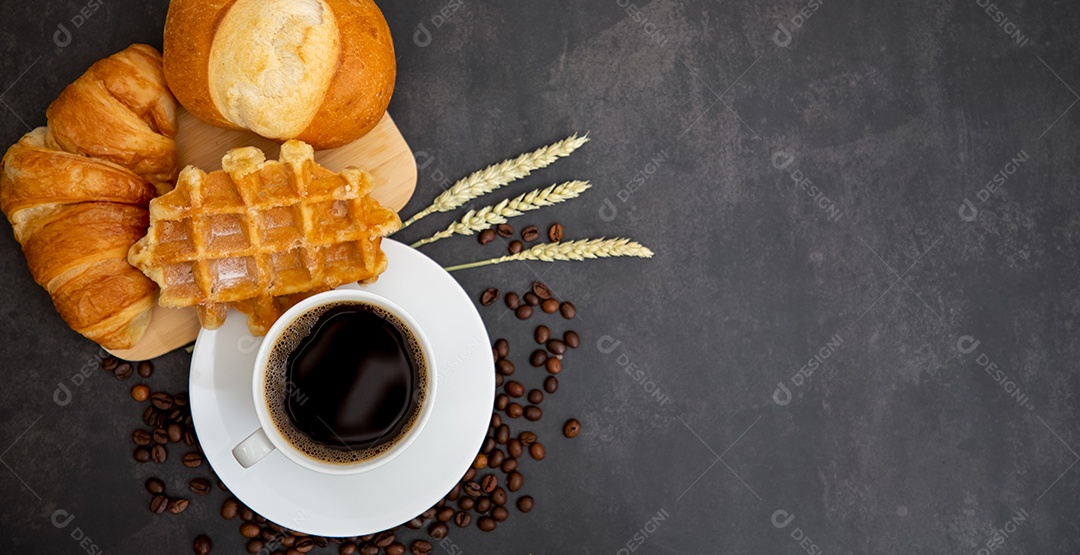 Café da manhã com uma xícara de café preto com pão com croissant e frutas na mesa de madeira.