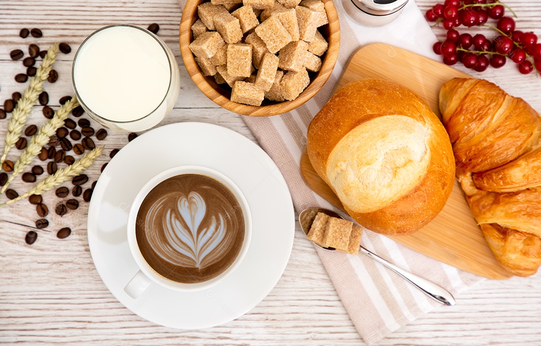 Café da manhã com uma xícara de café preto com pão com croissant e frutas na mesa de madeira.