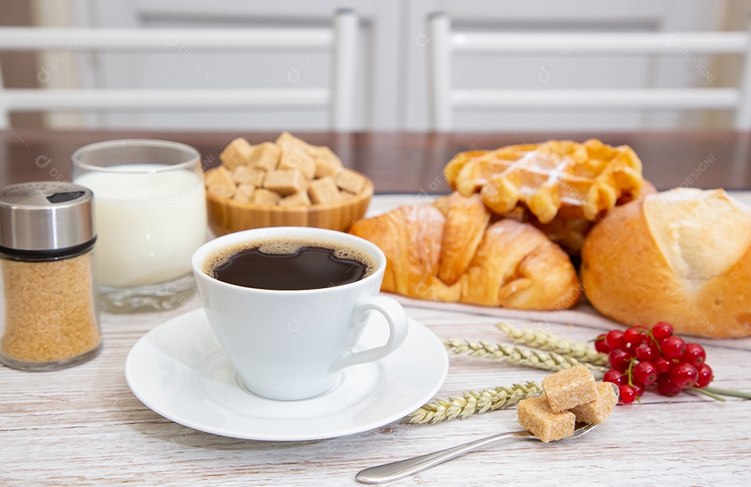 Café da manhã com uma xícara de café preto com pão com croissant e frutas na mesa de madeira.