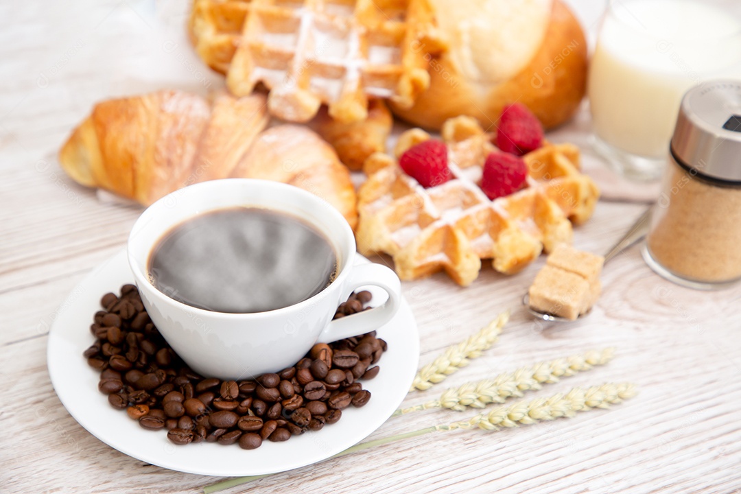 Café da manhã com uma xícara de café preto com pão com croissant e frutas na mesa de madeira.