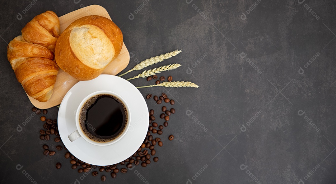 Café da manhã com uma xícara de café preto com pão com croissant e frutas no fundo preto.