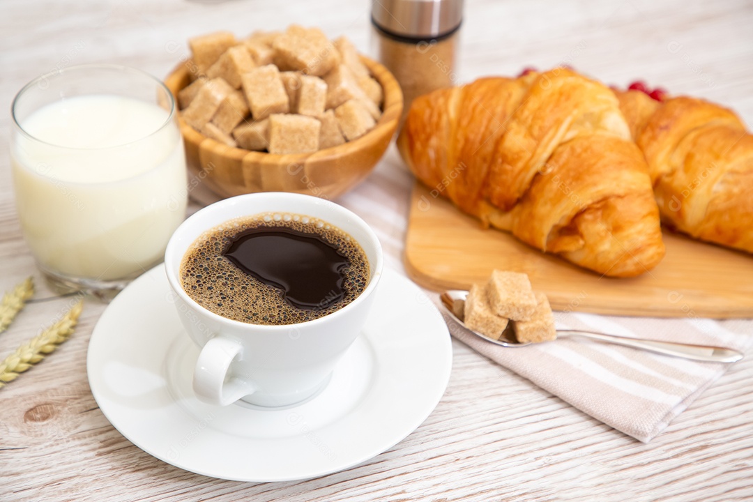 Café da manhã com uma xícara de café preto com pão com croissant e frutas na mesa de madeira.