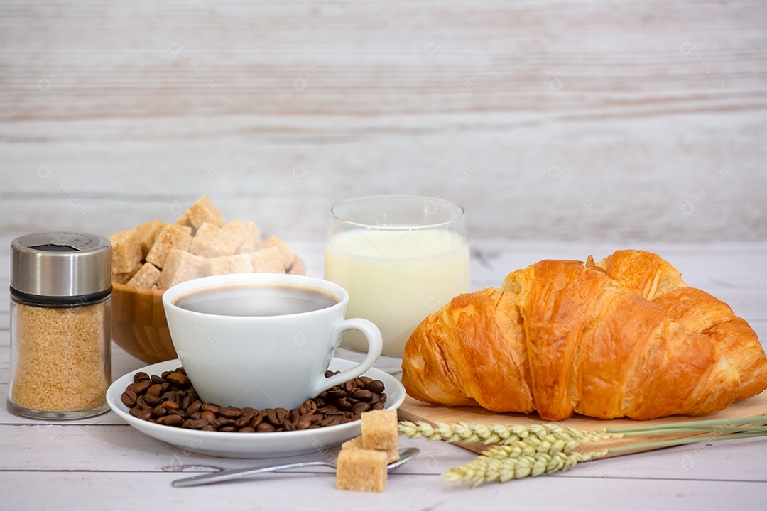 Café da manhã com uma xícara de café preto com pão com croissant e frutas na mesa de madeira.