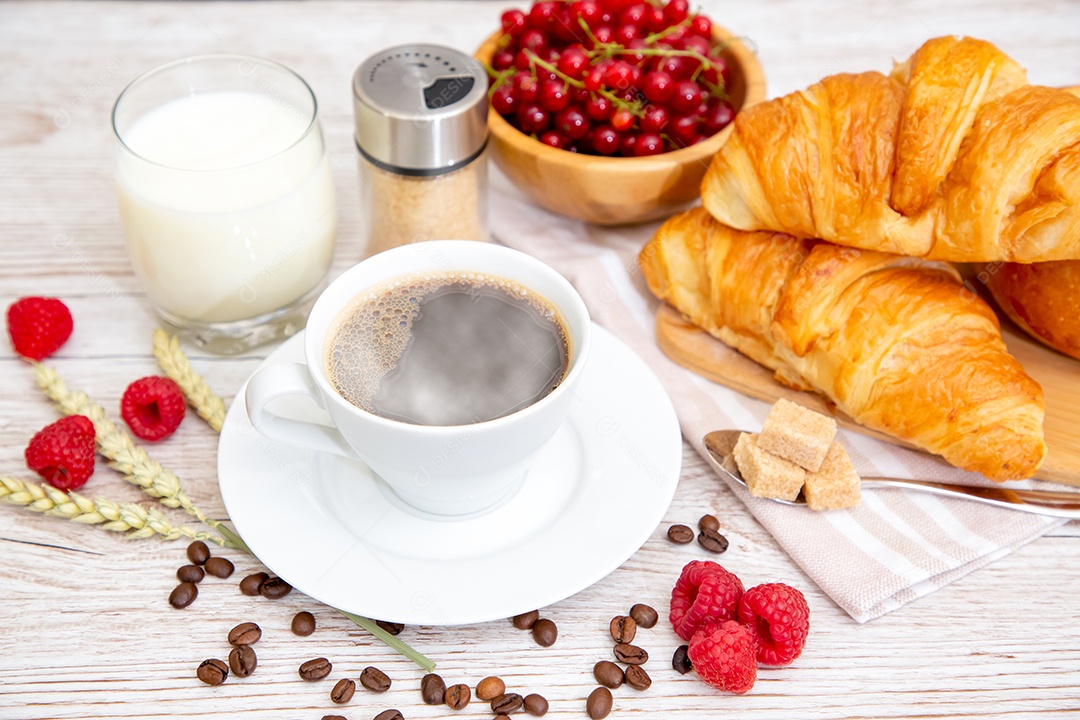 Café da manhã com uma xícara de café preto com pão com croissant e frutas na mesa de madeira.