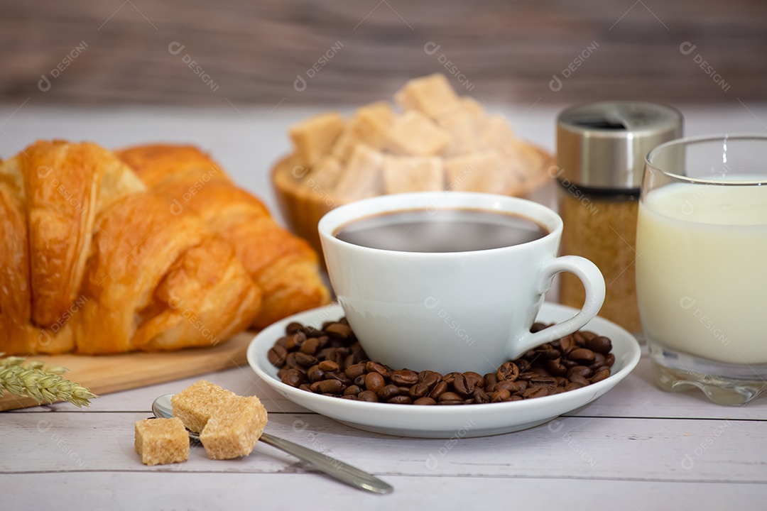 Café da manhã com uma xícara de café preto com pão com croissant e frutas na mesa de madeira.