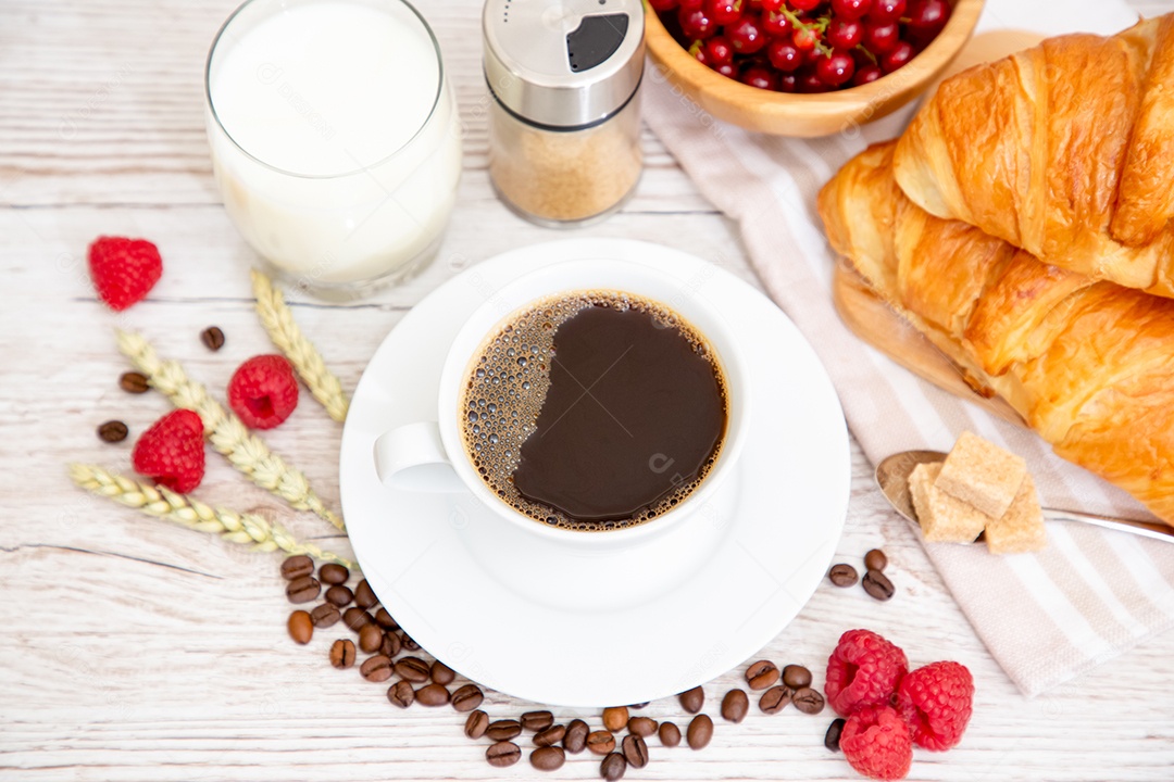 Café da manhã com uma xícara de café preto com pão com croissant e frutas na mesa de madeira.