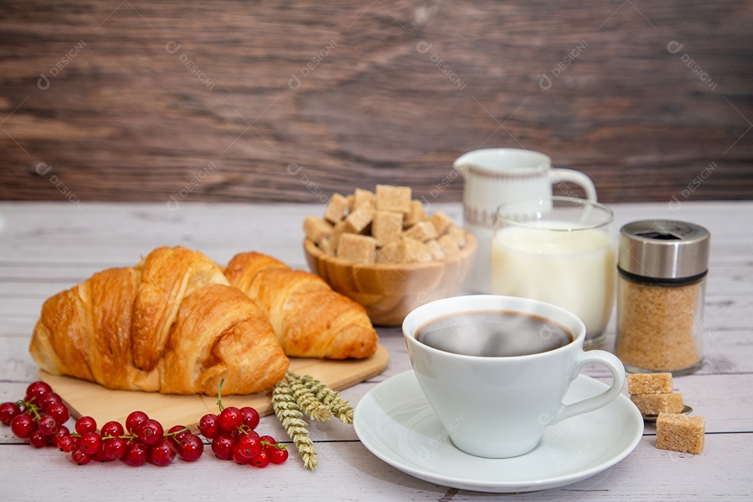 Café da manhã com uma xícara de café preto com pão com croissant e frutas na mesa de madeira.