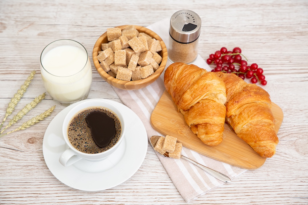 Café da manhã com uma xícara de café preto com pão com croissant e frutas na mesa de madeira