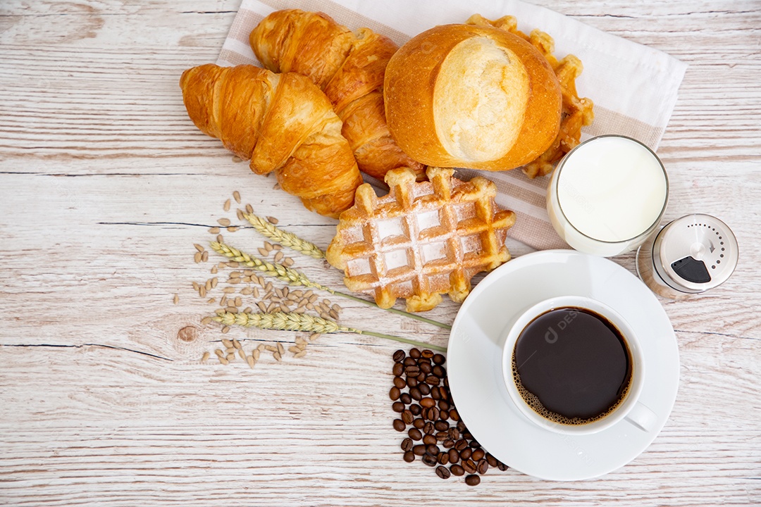 Café da manhã com uma xícara de café preto com pão com croissant e frutas na mesa de madeira.