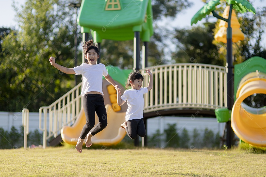 Duas meninas asiáticas se divertindo em um playground ao ar livre no verão