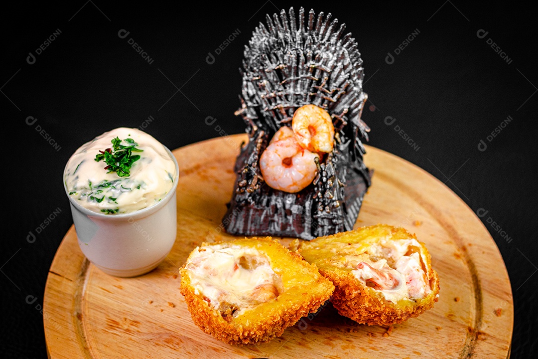 Imagem de coxinha sobre taboa de madeira e molho.