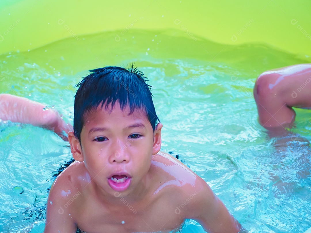 Um menino brincando na piscina e sorri feliz.