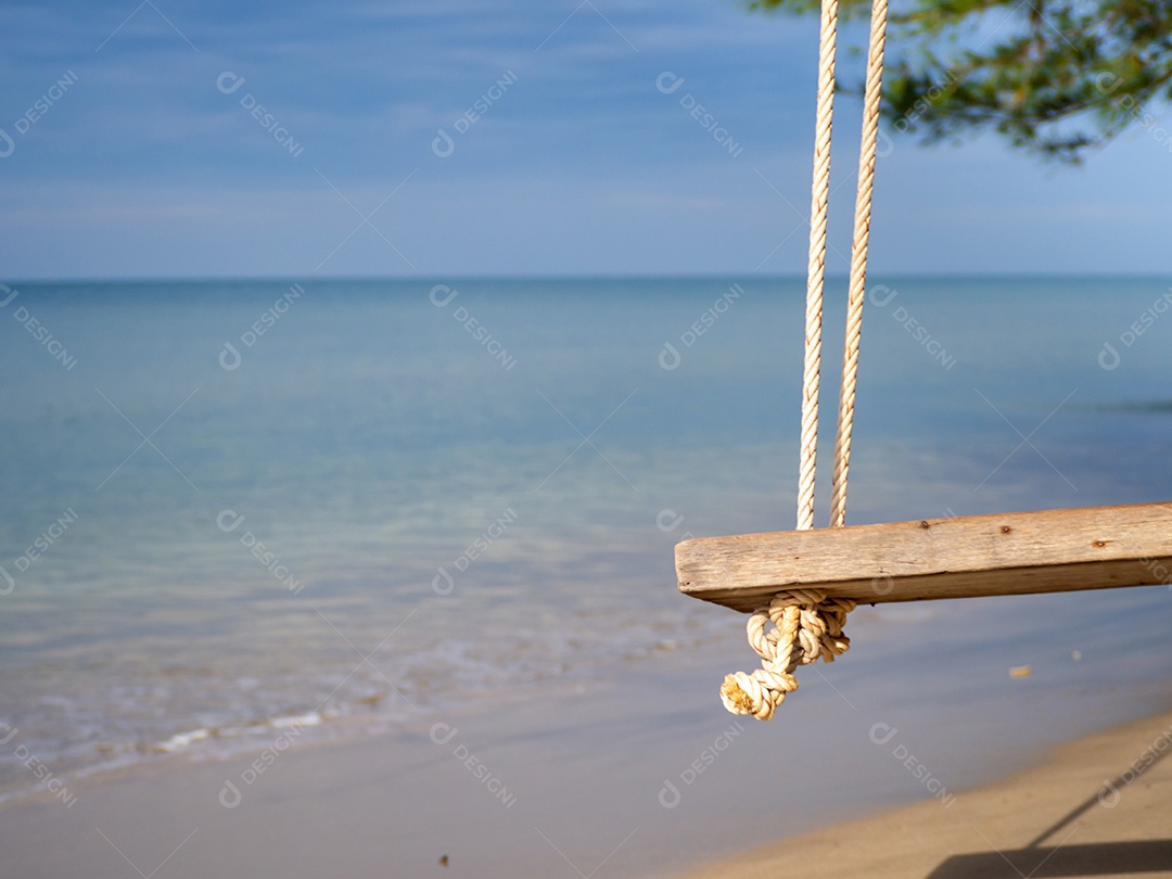 Balanço de madeira pendurado na árvore No fundo é um mar azul.