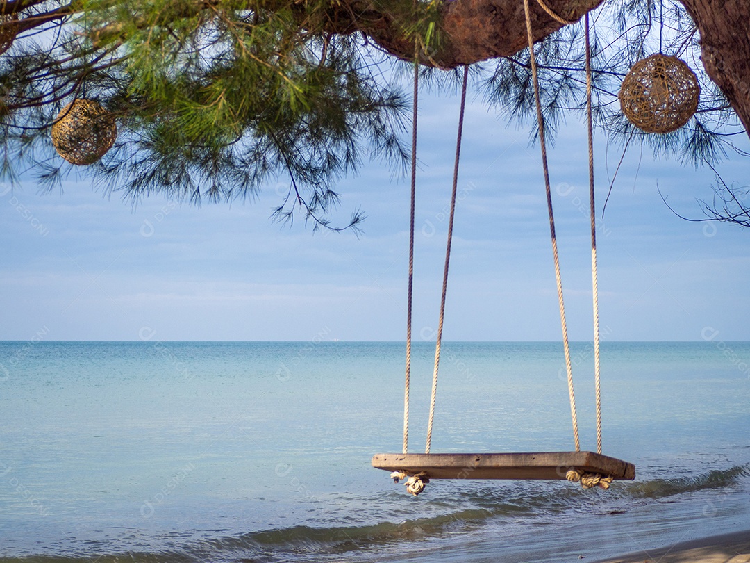 Balanço de madeira pendurado na árvore No fundo é um mar azul.