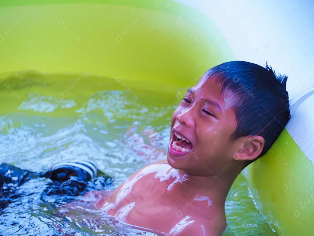 Um menino brincando na piscina e sorri feliz.