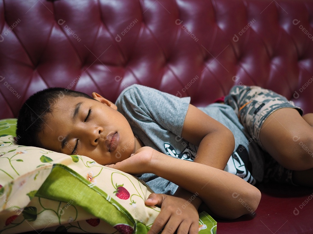 O menino adormeceu no sofá de couro vermelho.
