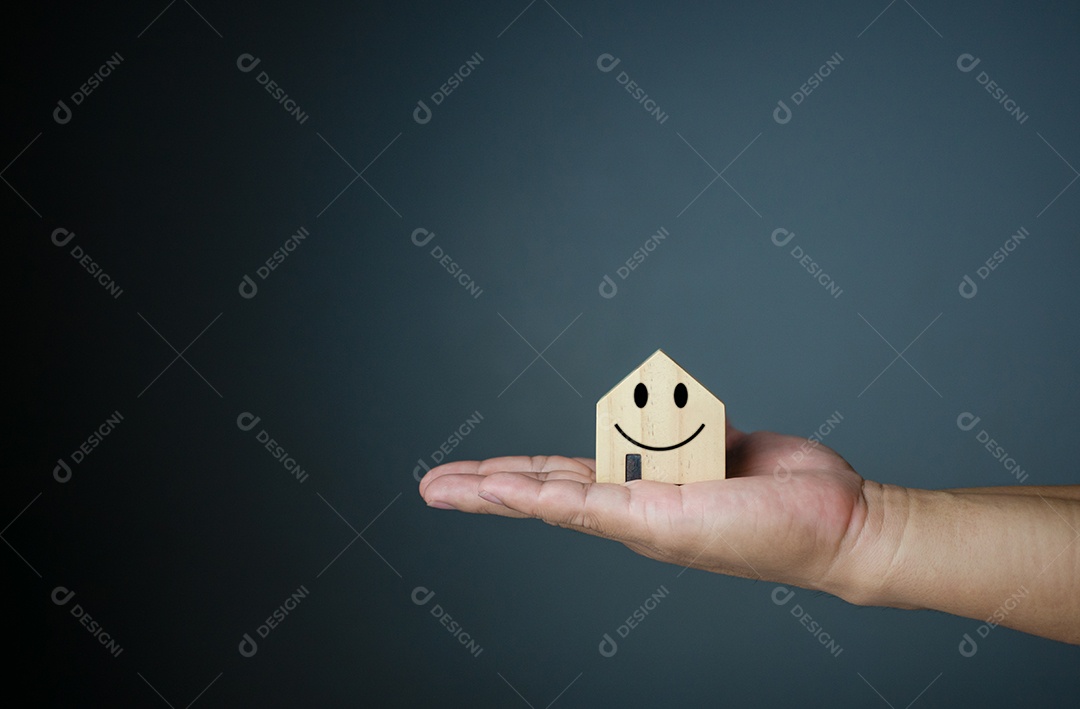 Conceito de casa feliz. Mão segurando uma casa modelo sorridente. Indica felicidade e amor na casa.