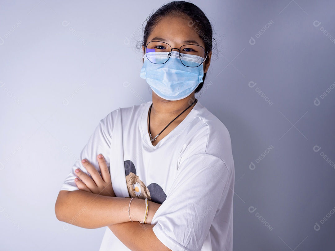 Menina vestindo uma máscara e usando óculos em pé com os braços cruzados.