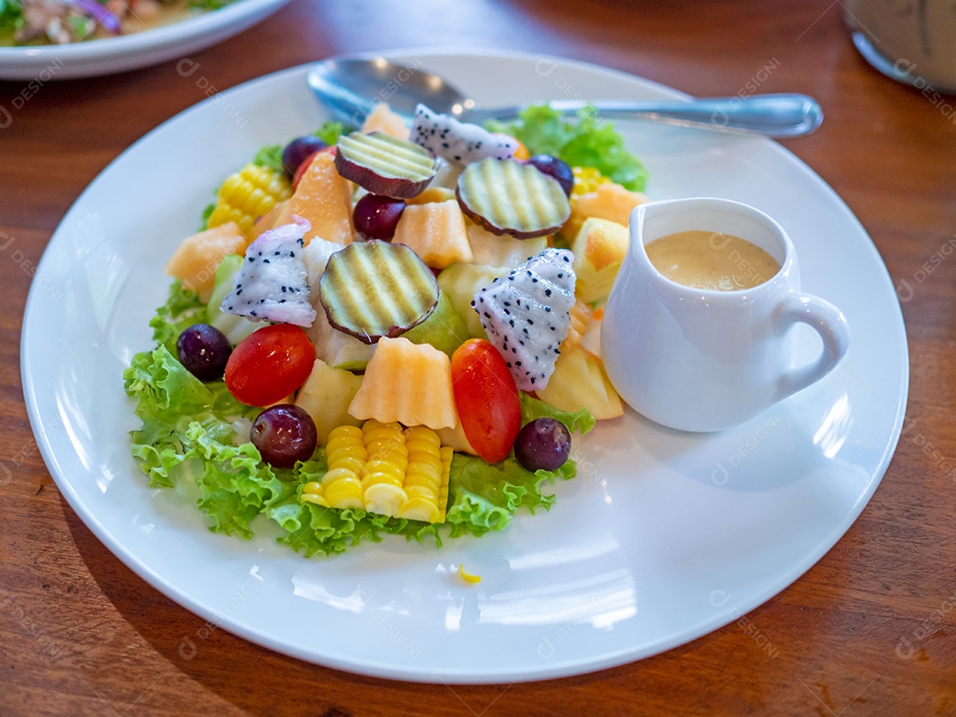 Salada de legumes em um prato branco colocado sobre um fundo de madeira.