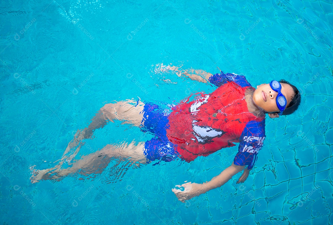 Menino vestindo um maiô e óculos nadando no meio da piscina.