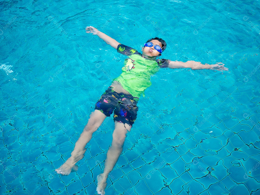 Menino vestindo um maiô e óculos nadando no meio da piscina.