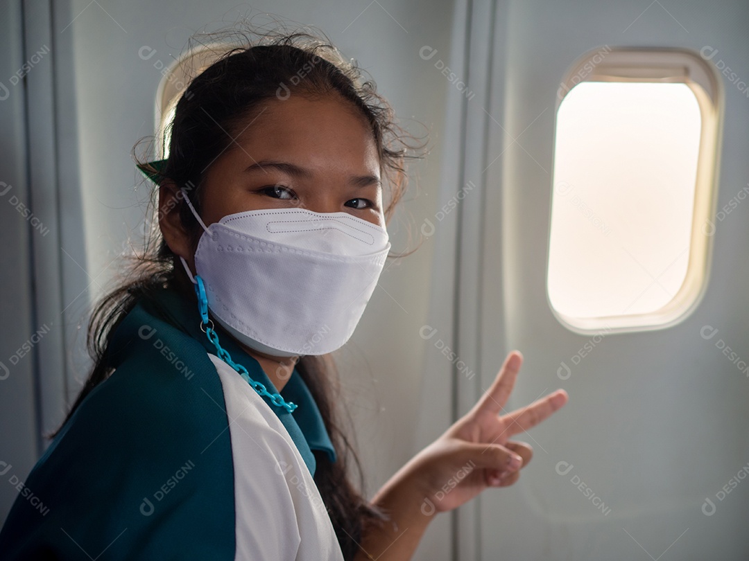 Uma mulher usando uma máscara está sentada perto da janela de um avião.