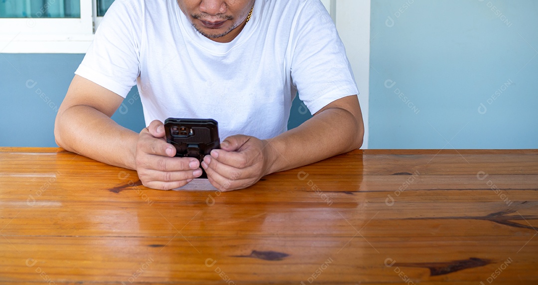 Homem asiático vestindo camisa branca usando o telefone em uma mesa de madeira.