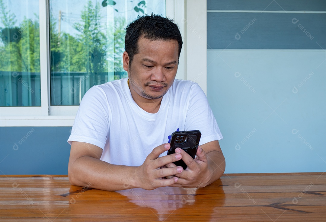 Homem asiático vestindo camisa branca usando o telefone em uma mesa de madeira.